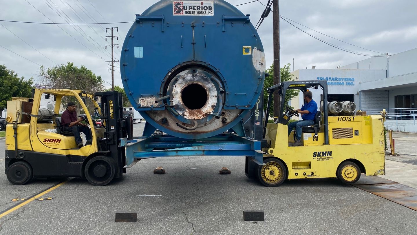 Two S.K. Machinery Moving forklifts carrying an industrial boiler at a dyeing and finishing plant